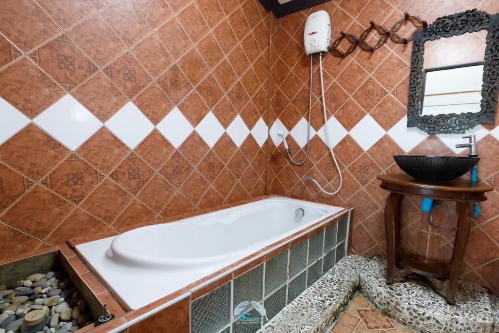 Bathroom with brown and white diamond-patterned tiles, a white bathtub, and a dark sink on a wooden stand.