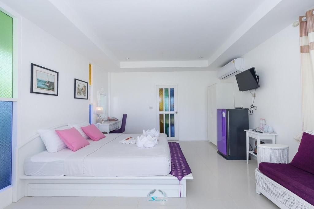 Bright hotel room with white walls, bed, purple accents, and a small television.