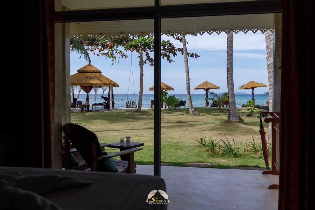 View from a room overlooking a beach with gazebos and palm trees; sea in the background.