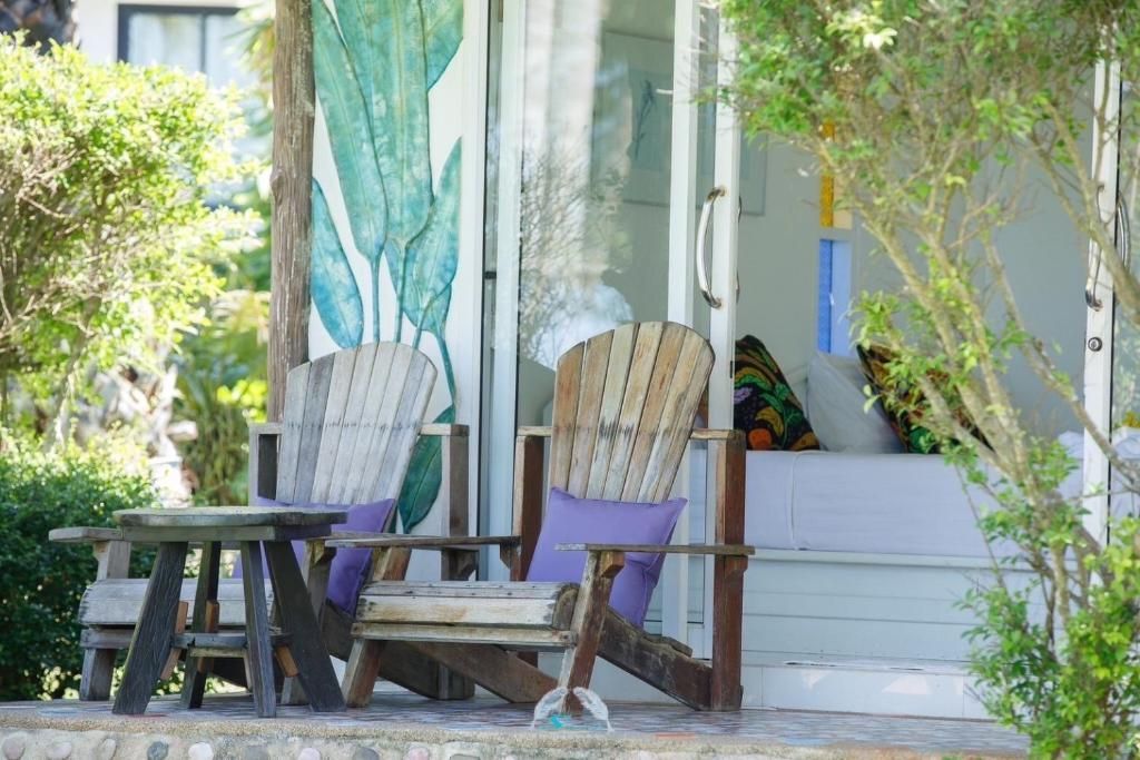 Two wooden chairs with purple cushions sit outside a building with glass doors, a small table between them.