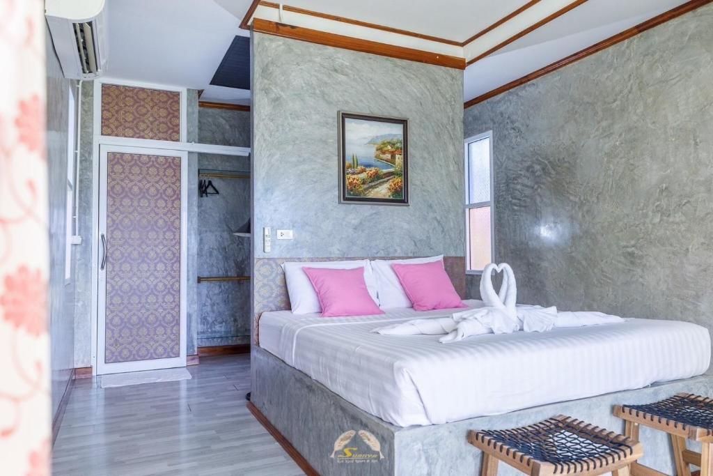 Bedroom with a gray concrete wall, a bed with pink pillows and white towels shaped as swans.