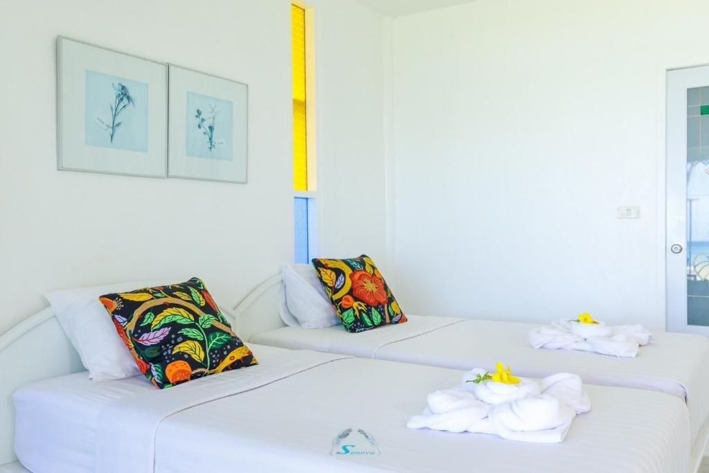Two twin beds in a bright white room, adorned with colorful pillows and artwork.