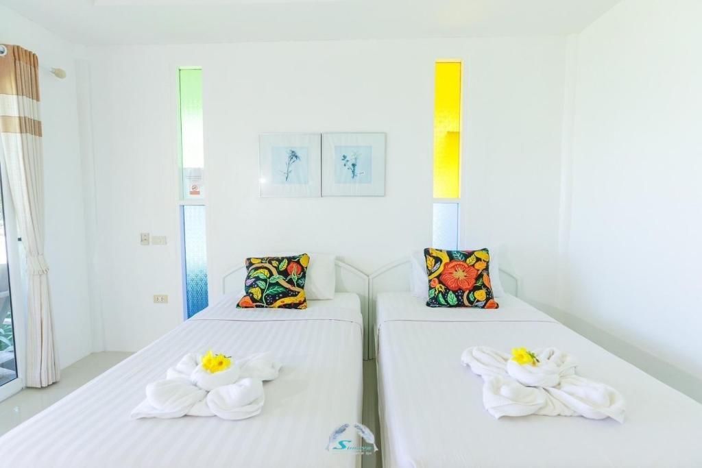 Two twin beds in a bright white room, adorned with colorful pillows and folded towels.