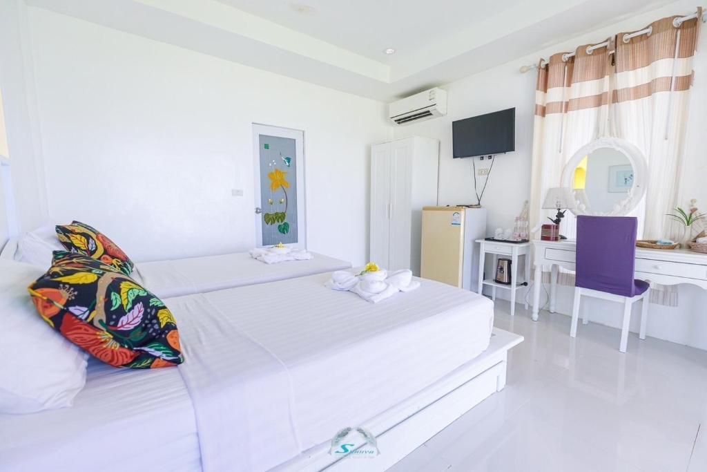Bright white bedroom with twin beds, TV, vanity, and a small fridge.