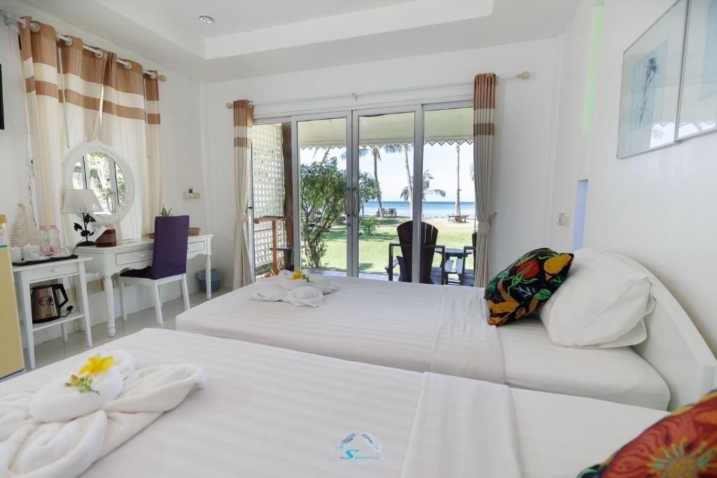Bright hotel room with two beds, a vanity, and a balcony overlooking a beach.