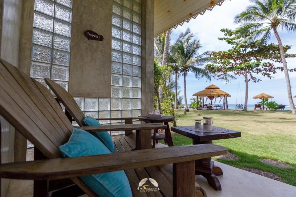 Wooden chairs on a porch overlooking a beach with palm trees and a gazebo.