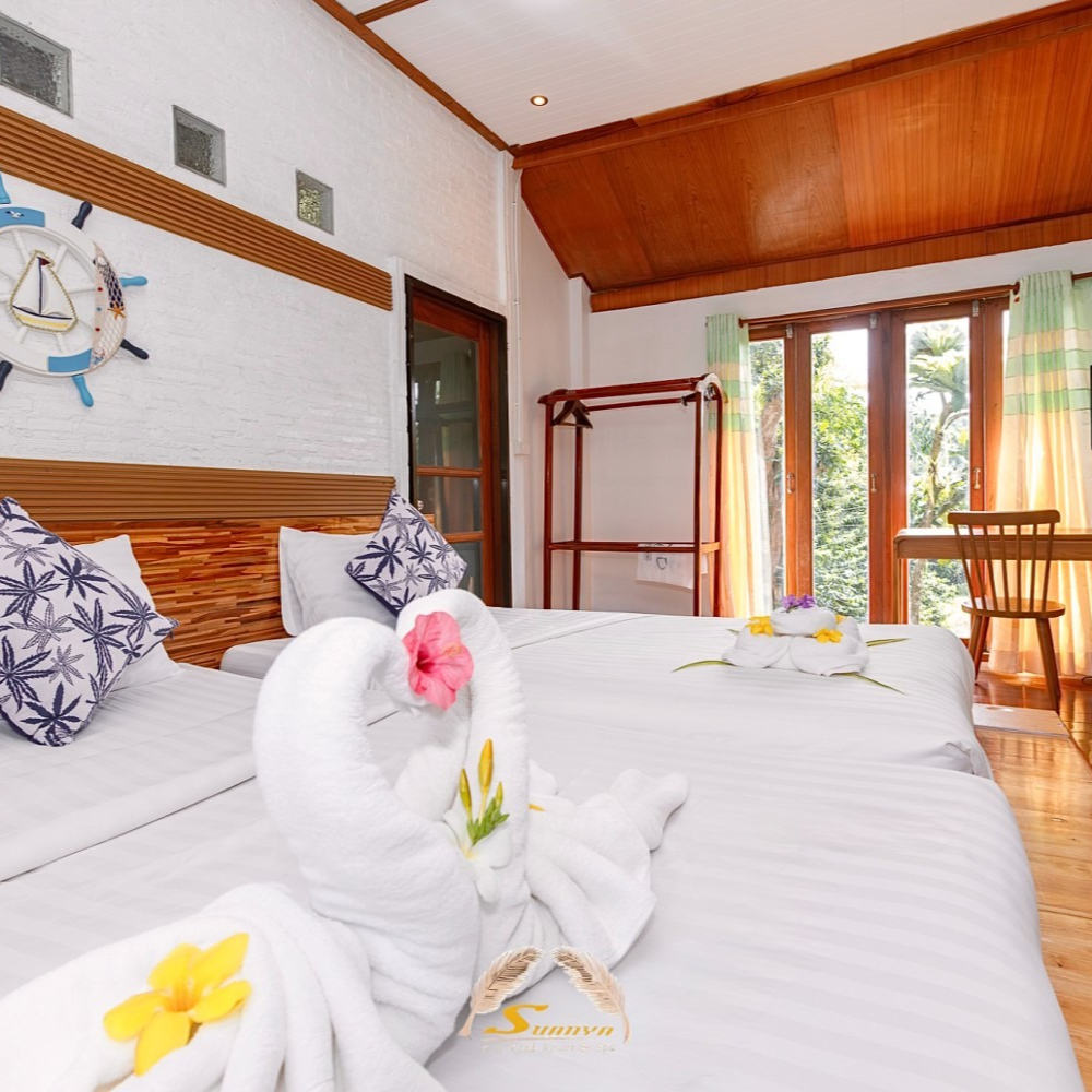 Cozy hotel room with two beds, decorated with towel swans and pillows, wooden decor, and a view.