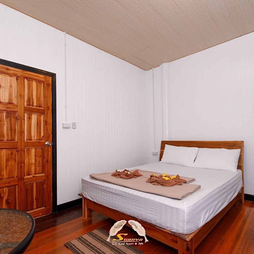 Bedroom with wooden door, bed, and floor. White walls, tan blanket, and brown rug.