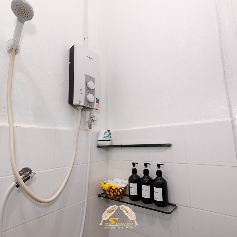 Shower with a water heater, shampoo bottles, and a shelf in a white tiled bathroom.