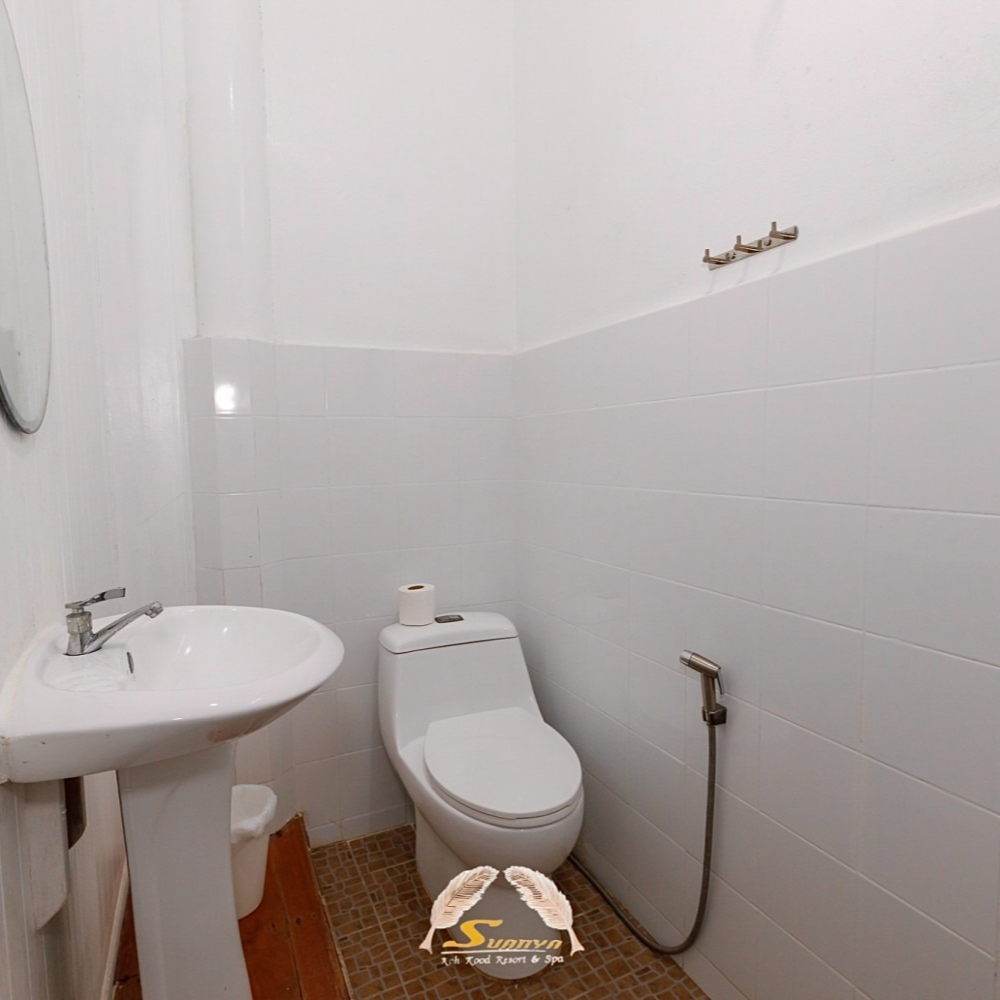 A small, white-tiled bathroom with a pedestal sink, toilet, and handheld bidet.