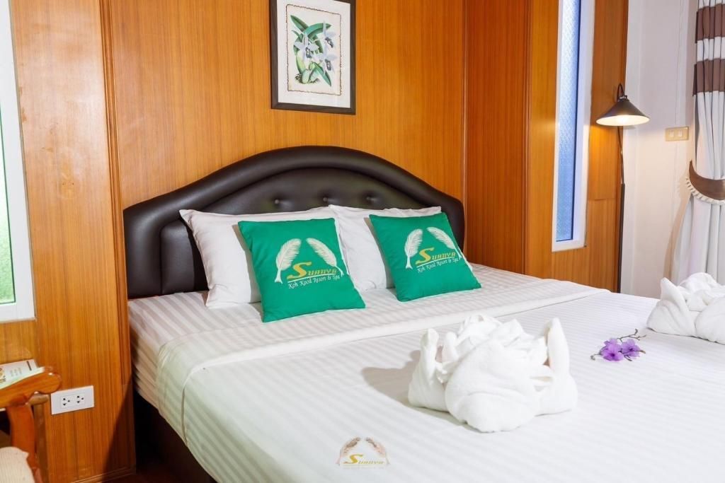 Cozy hotel room with a made bed, two green pillows, and wooden paneling.