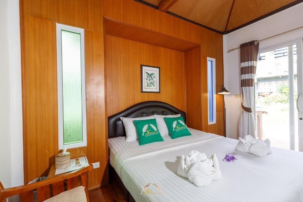Bedroom with wooden paneling, queen bed with green pillows, towels folded as elephants.