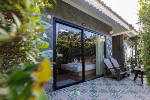 Sliding glass door to a room with a bed, two chairs, and a small table on a tiled patio.