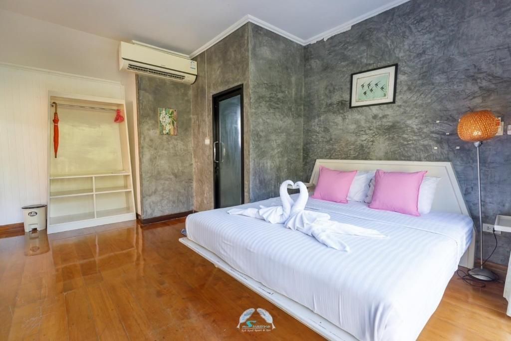 Bedroom with bed, pillows, swan towels, textured walls, and wood floor.