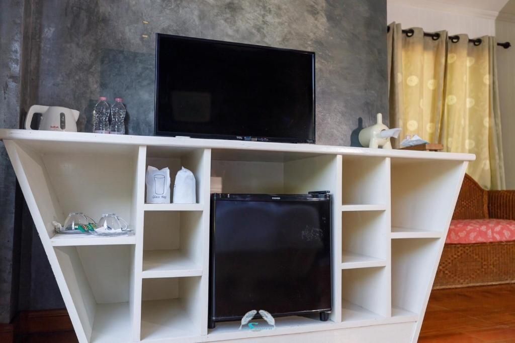White cabinet with TV, small fridge, and decorative items in a room with curtain and grey wall.