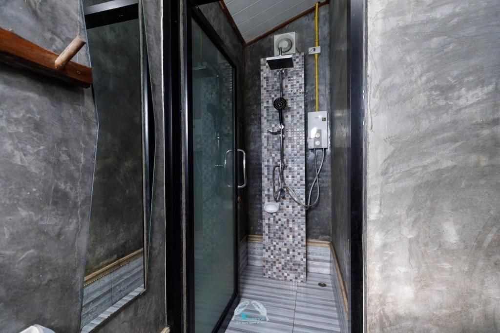 A small, modern bathroom with a stone shower column, glass door, and gray concrete walls.
