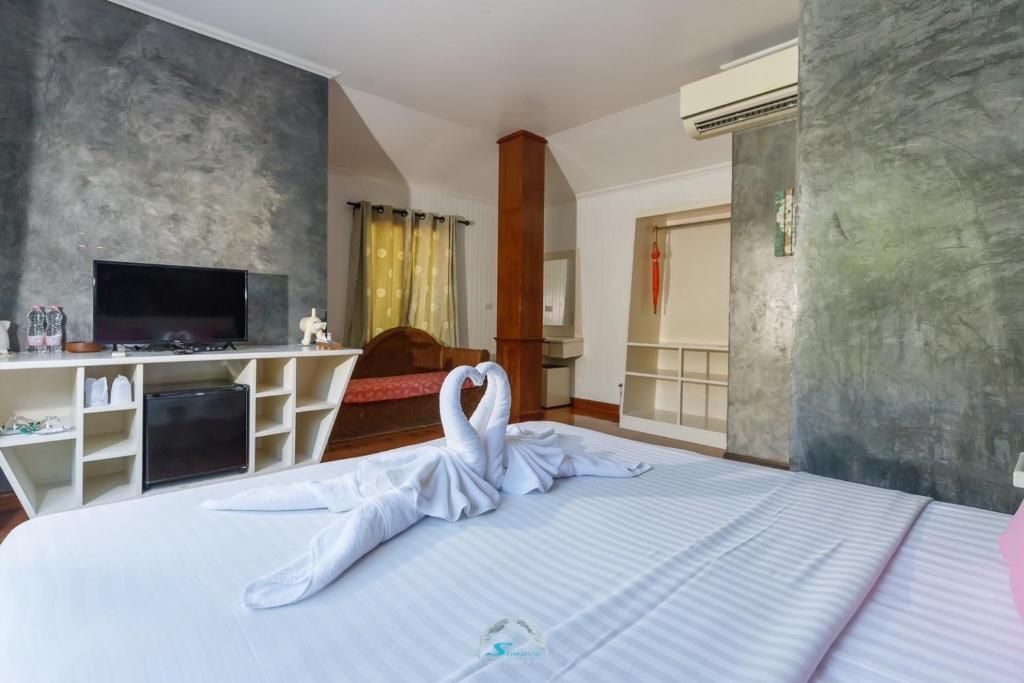Bedroom with swan towel art on the bed, TV, and air conditioner; concrete wall backdrop.