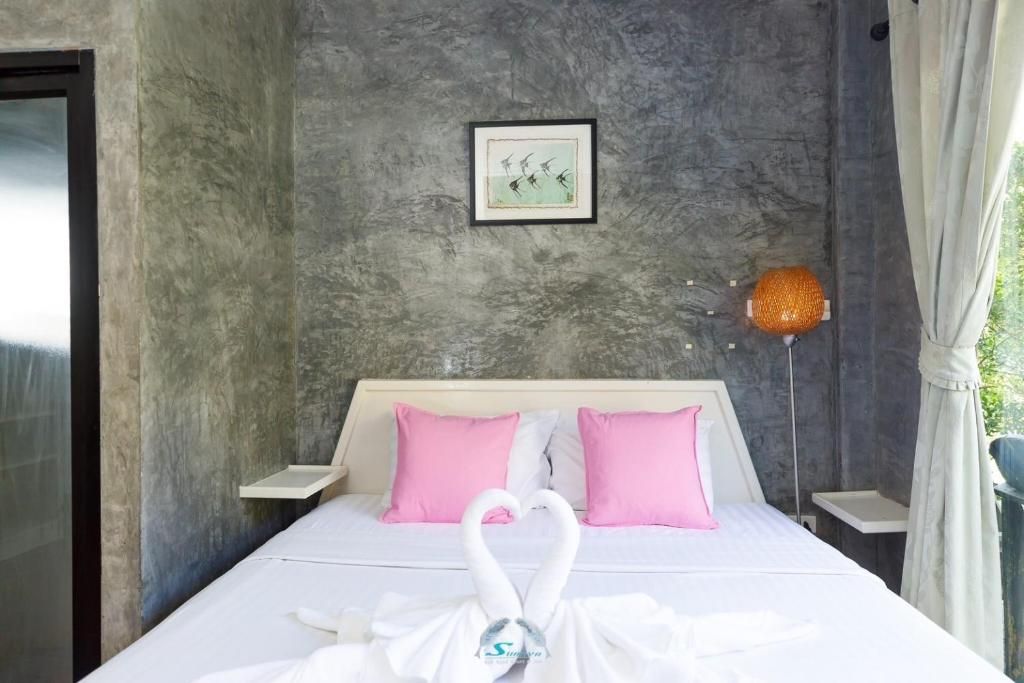 Bedroom with white bedding, pink pillows, and swan towels, against a gray concrete wall.