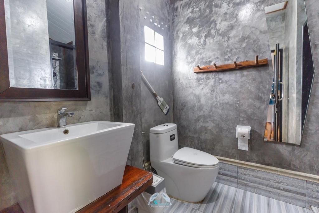 Modern bathroom with gray concrete walls, white sink, toilet, and striped tile floor.