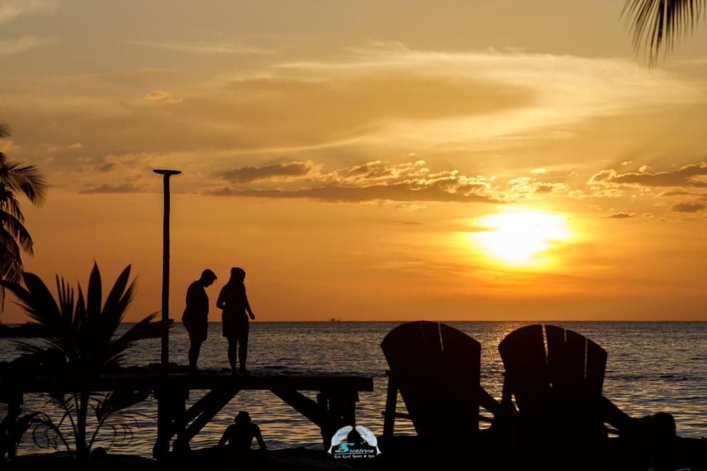 Silhouette of people on a pier at sunset; two chairs in foreground facing the ocean.