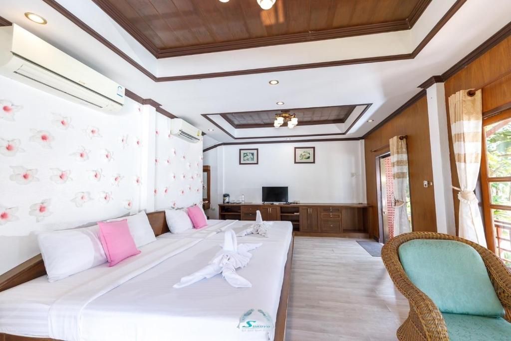 Hotel room with large bed, floral wallpaper, wooden ceiling and walls, and a wicker chair.