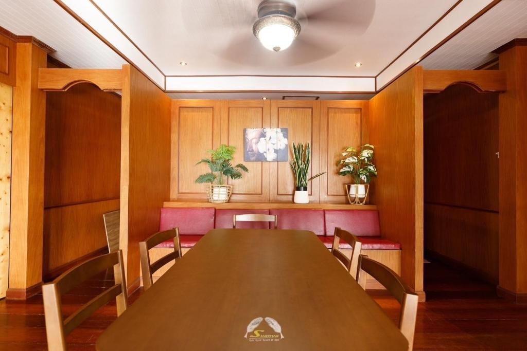 Wooden dining room with long table, built-in bench seating, plants, and ceiling fan.