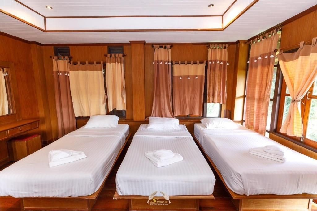 Three twin beds in a wood-paneled room with curtains and a window.