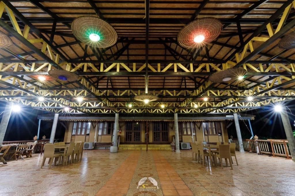 Open-air restaurant patio with tables, chairs, and thatched roof with decorative lights.