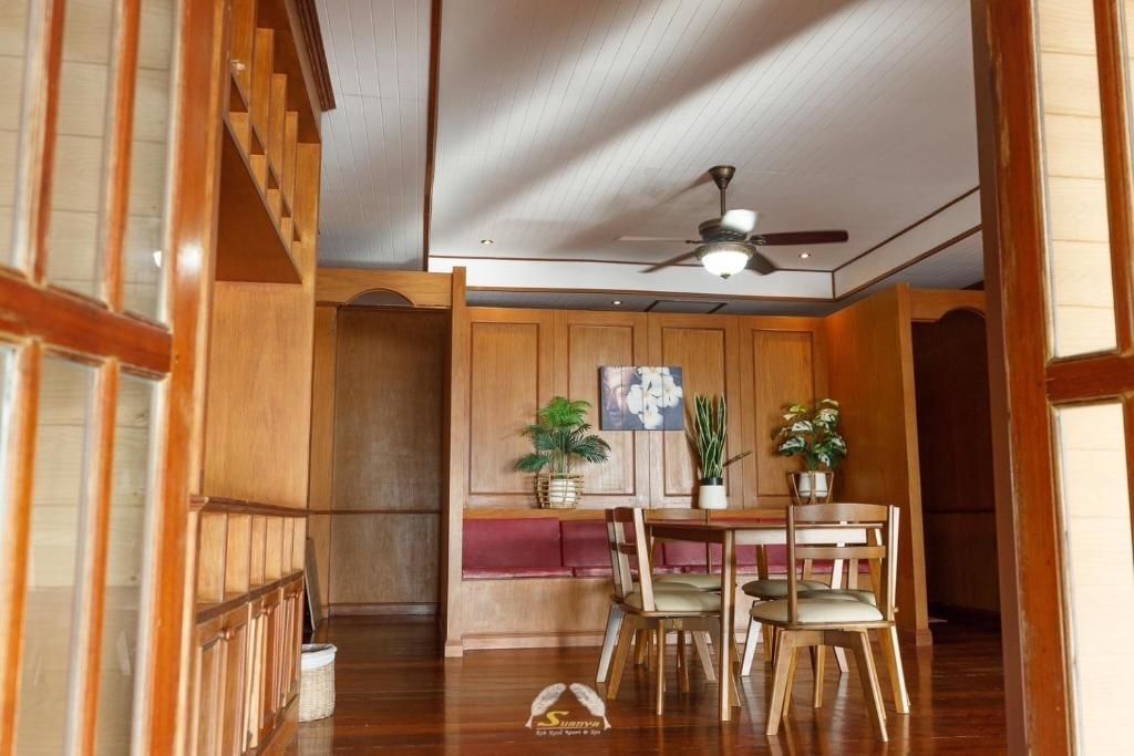Wooden dining room with table, chairs, and plants; view through doorway.