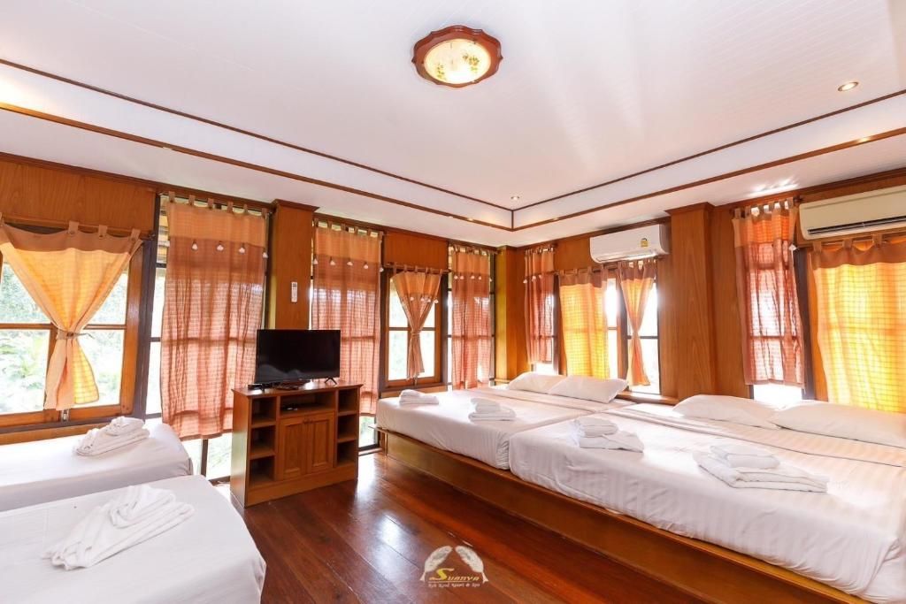 A bedroom with four beds, wood paneling, and large windows with orange curtains.