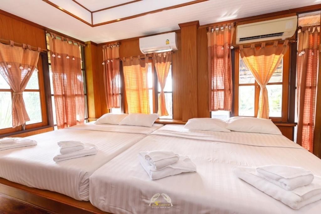 Bedroom with two beds, wooden paneling, orange curtains, and air conditioning units.