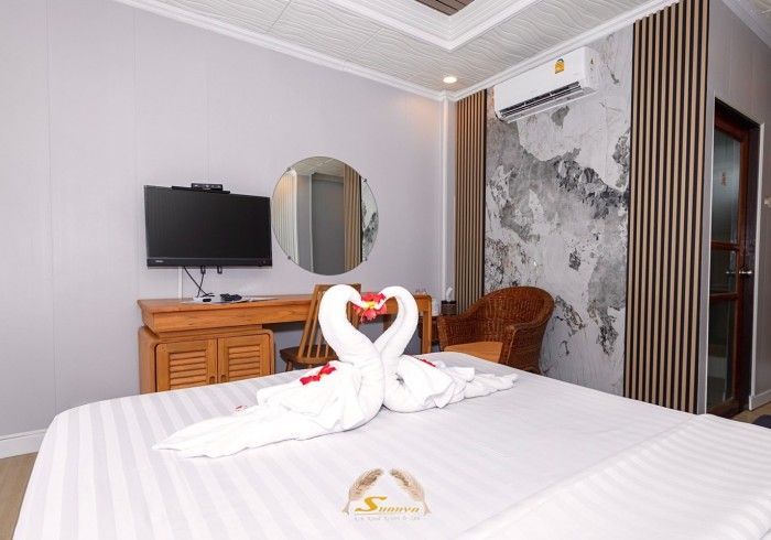 Hotel room with bed, TV, desk, mirror, swan towel art. Wall decor: wood, patterned stone.
