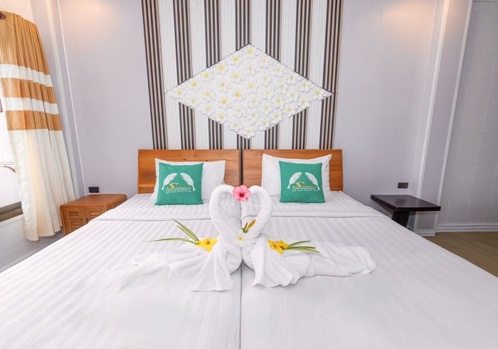 Bedroom with large bed, decorative swan towels, green pillows, and wooden headboard.
