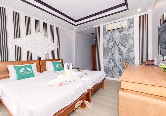 Hotel room with twin beds, white bedding, wooden furniture, and marble accent wall.