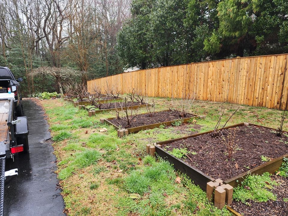 A wooden fence surrounds a garden with a trailer parked in front of it.