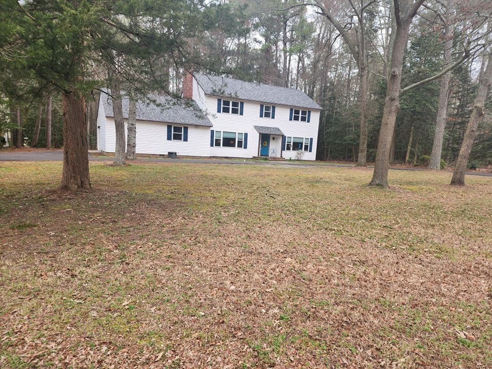 A large white house is sitting in the middle of a lush green field surrounded by trees.