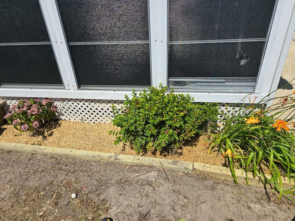 A screened in porch with flowers and bushes in front of it.