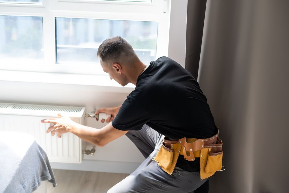 Un homme répare un radiateur dans une chambre.