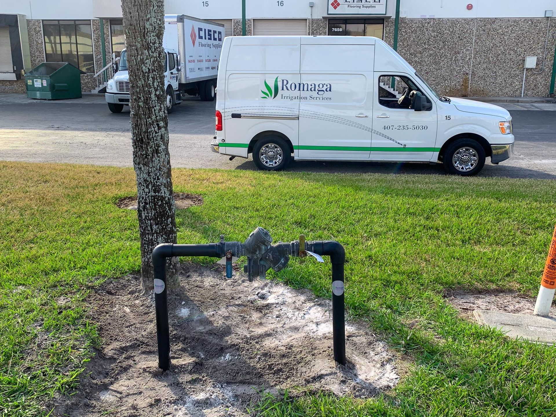 A white van is parked on the side of the road next to a tree.