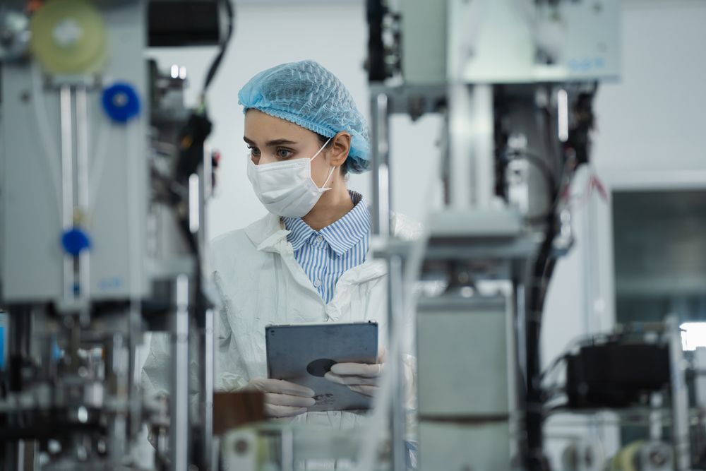 A female scientist wearing a mask is using a tablet in a laboratory.