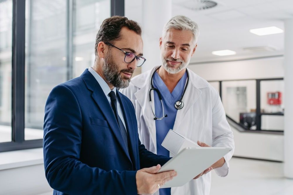 A man in a suit and tie is looking at a tablet with a doctor.