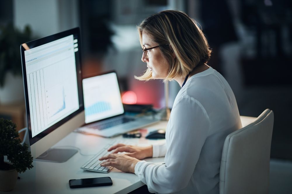 A woman is sitting at a desk typing on a computer.