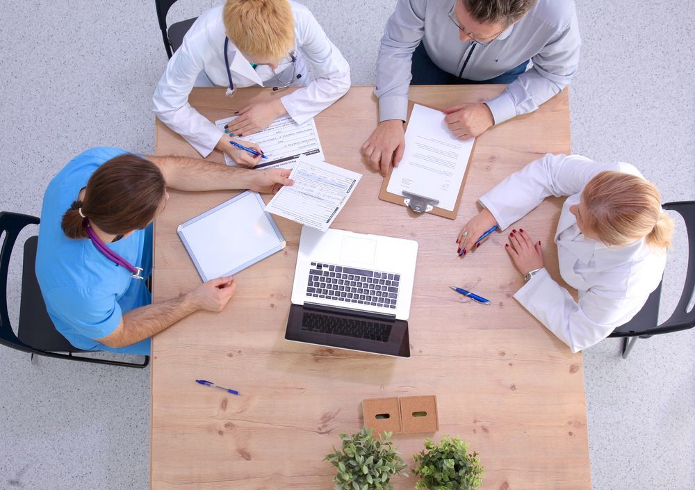 A group of doctors are sitting around a table with a laptop.