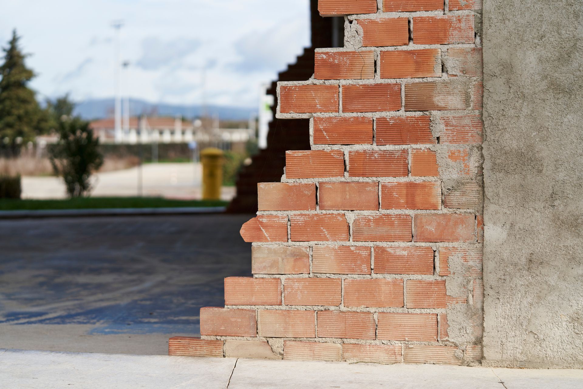 Brick wall, partially demolished, reveals a concrete pillar.