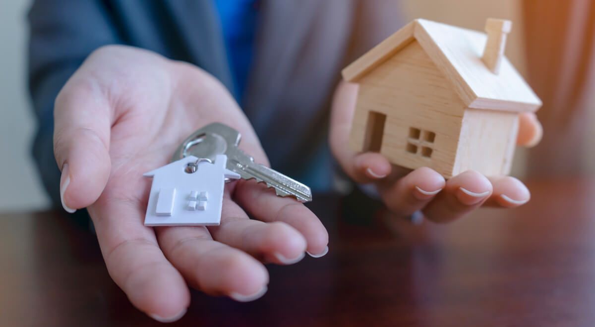 A person is holding a key and a model house in their hands.