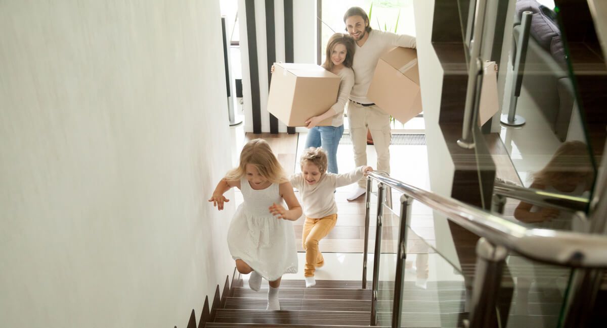 A family is moving into a new home and carrying boxes down the stairs.