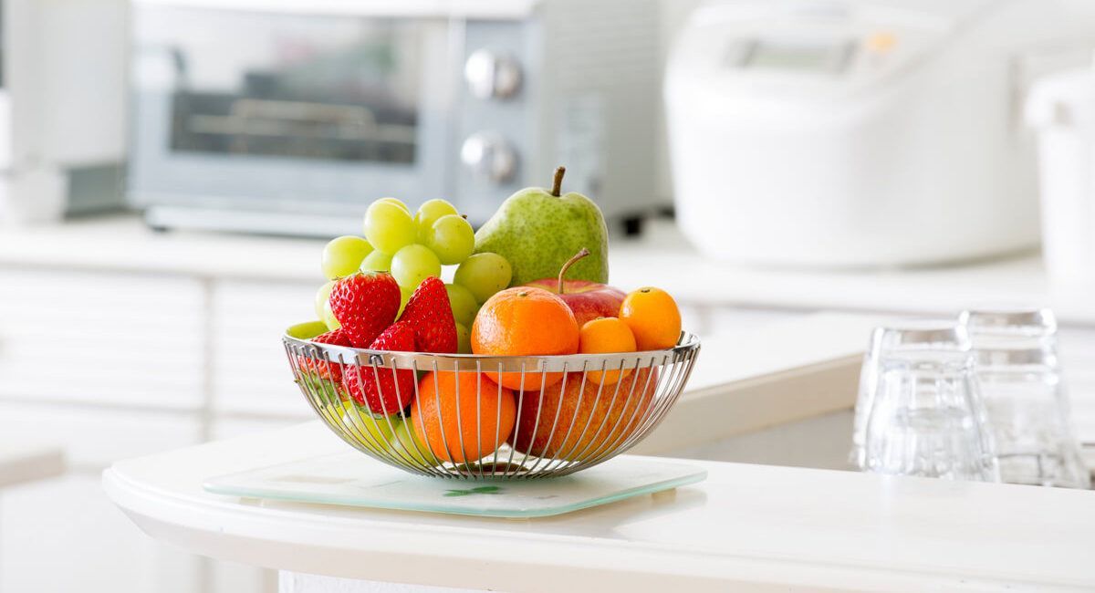 A bowl of fruit is sitting on a counter in a kitchen.