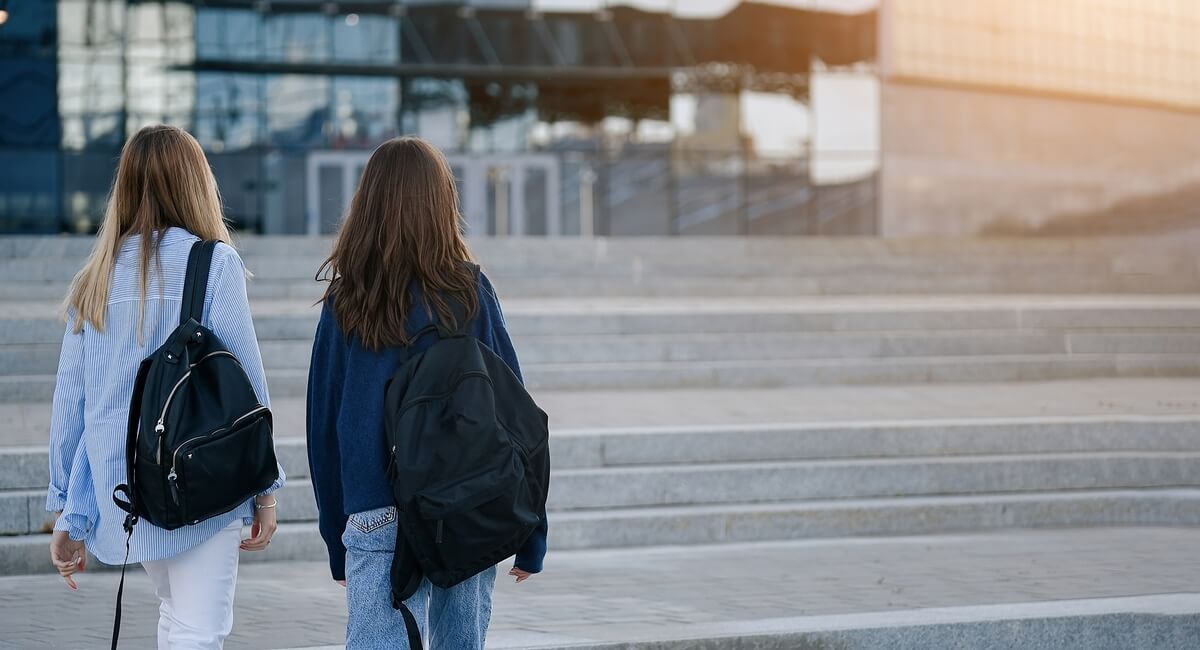 Two girls with backpacks are walking down the stairs.