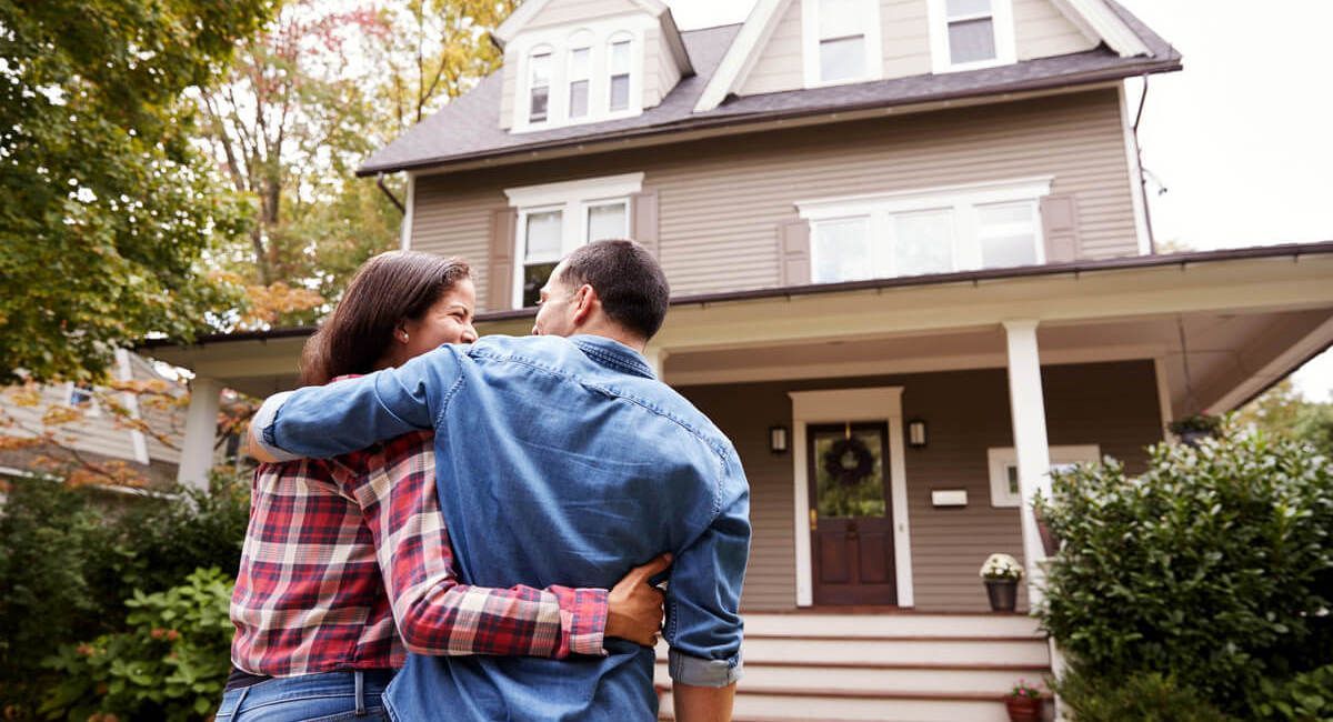 A man and a woman are hugging in front of a house.