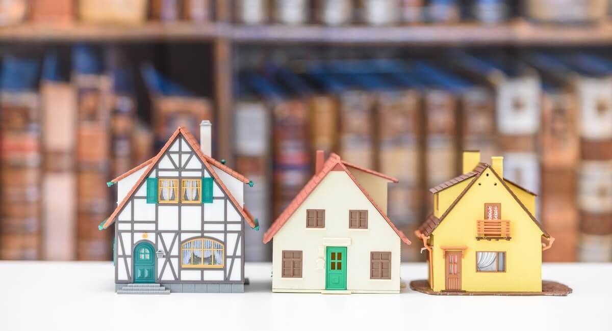 Three small houses are sitting on a table in front of a bookshelf.